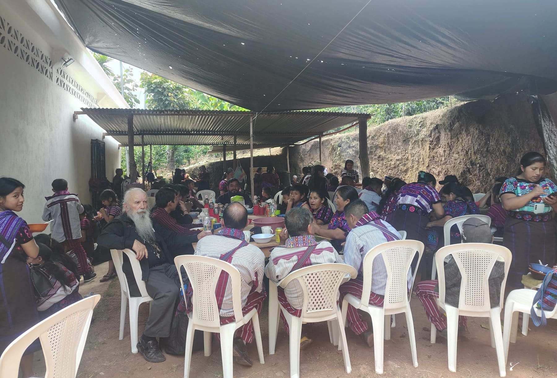Parishioners and clergy sharing a meal at long tables under a tarp